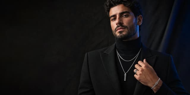 Man in black tailoring wearing layered silver jewelry